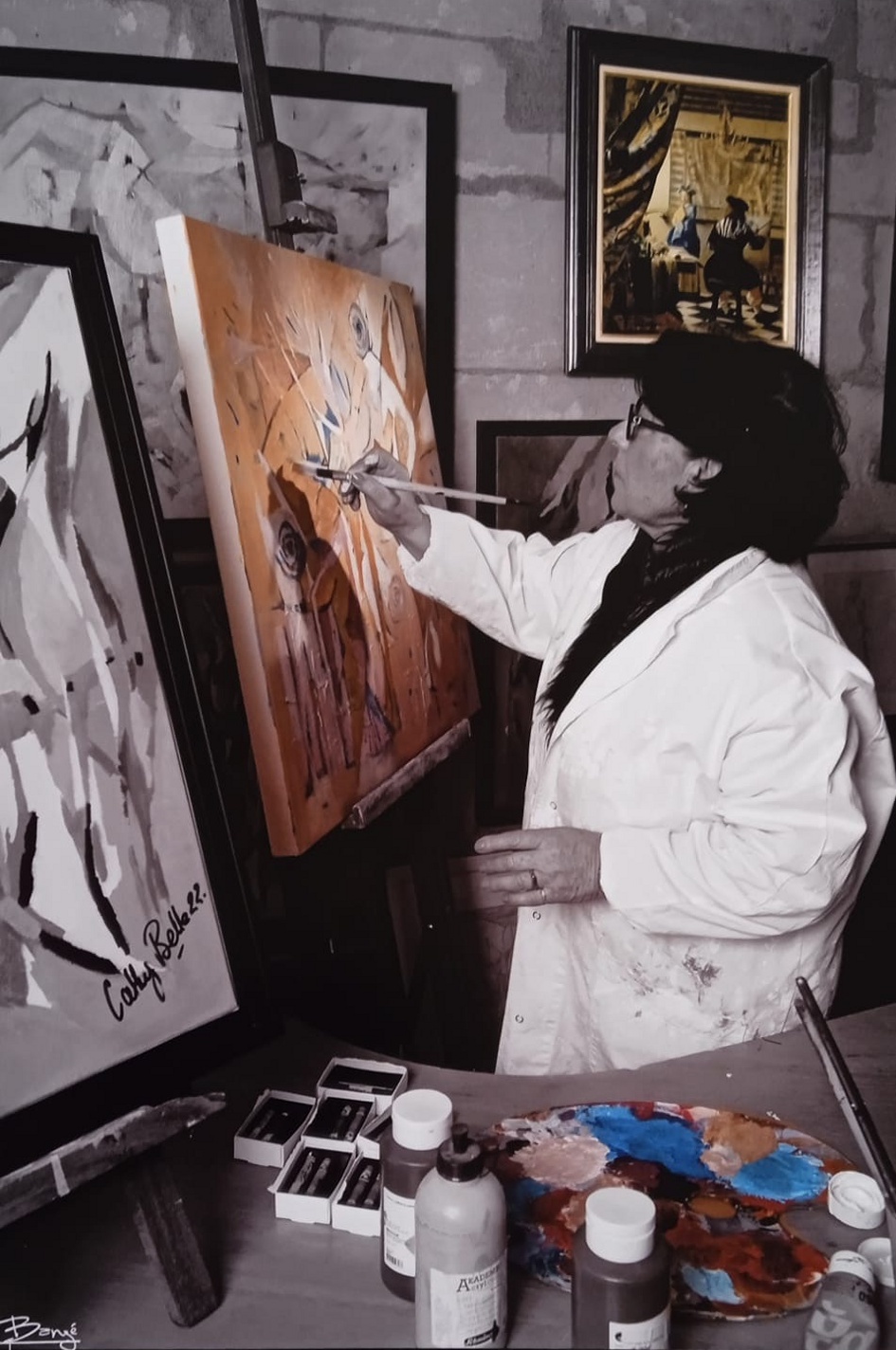 Cathy Belle peignant à son chevalet dans son atelier, entourée de tableaux et de sa palette